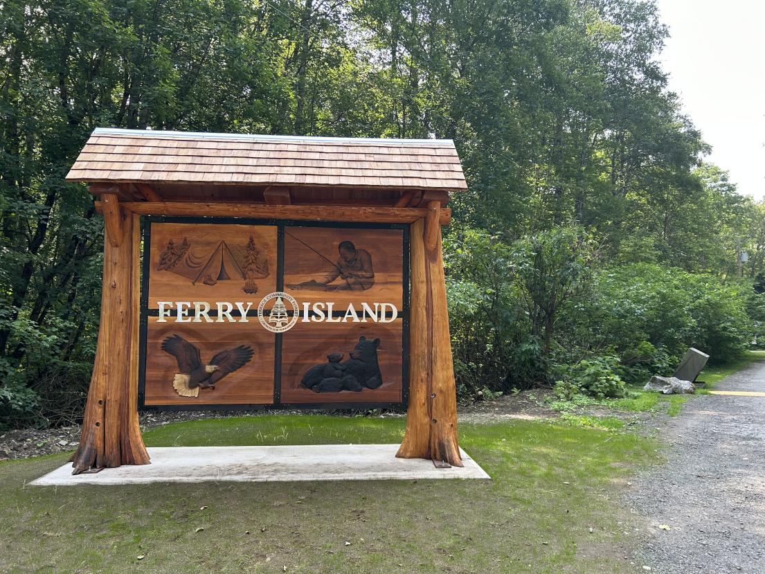 a photo of the new carved wooden sign at Ferry Island, featuring images of nature including an eagle and bear