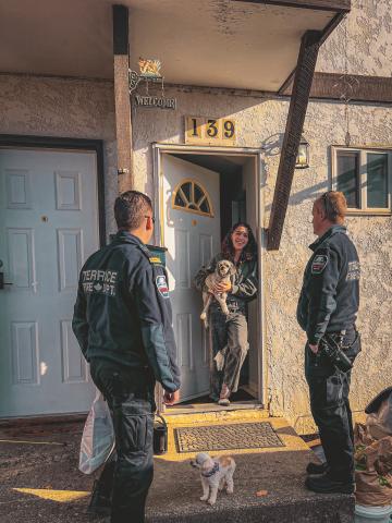 a photo of a woman and her dogs at their front door, talking to two firefighters